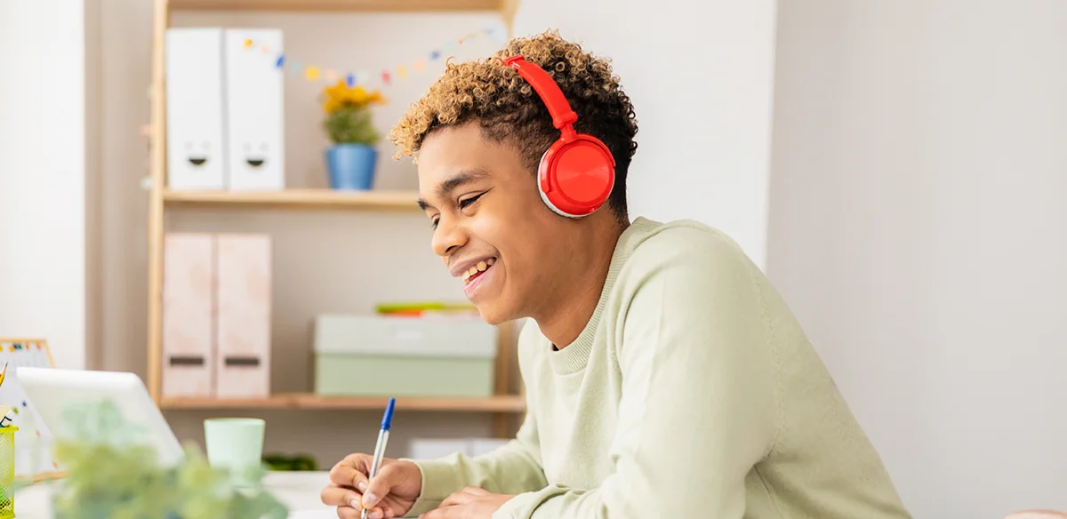 Student taking notes wearing a orange paif of headphones